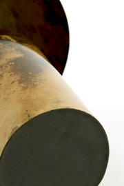 Detailopname vanuit laag perspectief van de onderzijde van een goudkleurig metalen object met ronde zwarte voet en karaktervolle verweerde afwerking