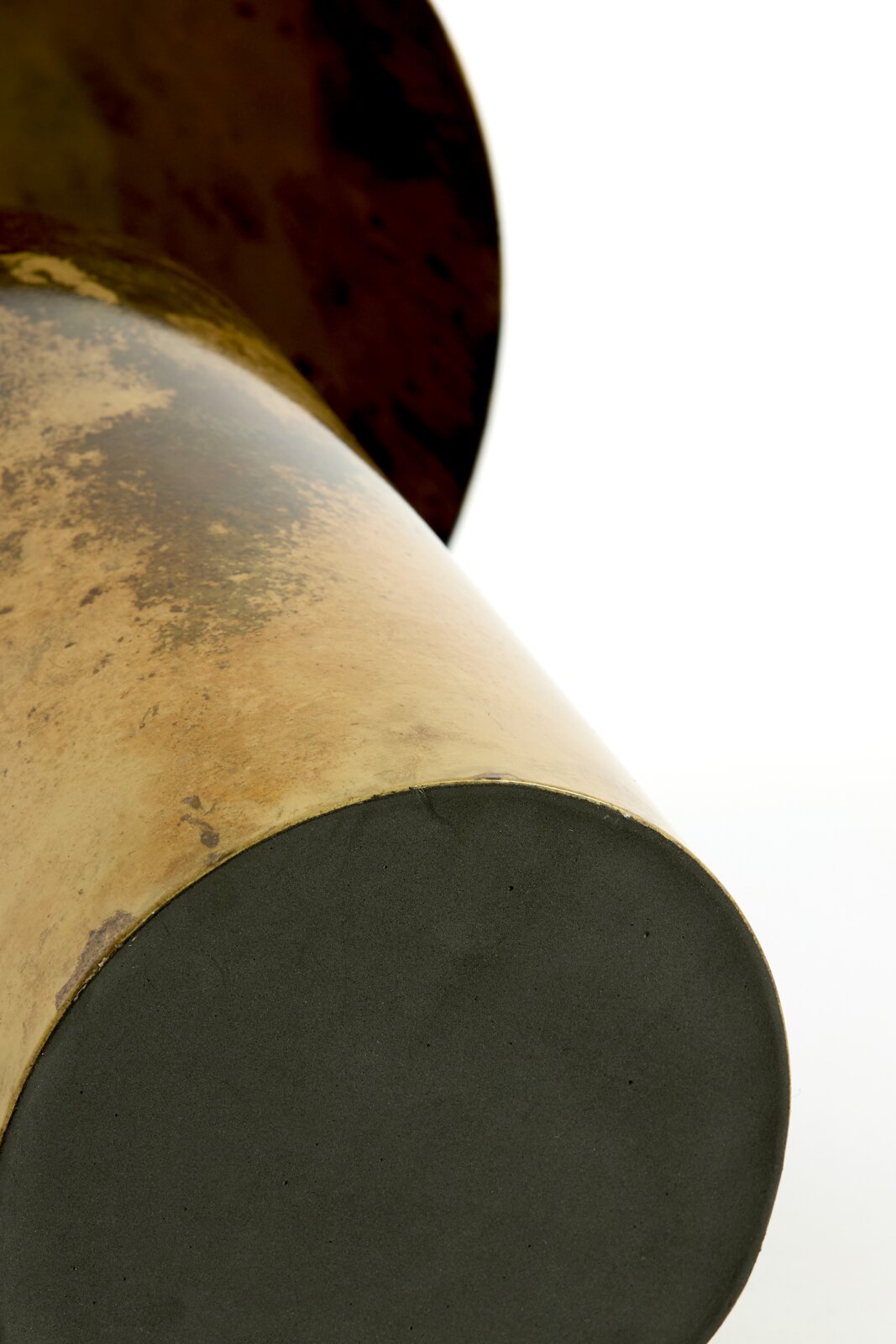 Detailopname vanuit laag perspectief van de onderzijde van een goudkleurig metalen object met ronde zwarte voet en karaktervolle verweerde afwerking