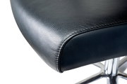 Nahaufnahme eines schwarzen Ledersitzes eines Chefsessels mit verchromtem Fußgestell, seitliche Perspektive.