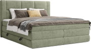 Groen gestoffeerd boxspringbed met hoog, rechthoekig gecapitonneerd hoofdbord, opgemaakt met grijs beddengoed en kussens, schuin van voren gefotografeerd.