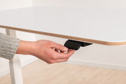 Nahaufnahme eines weißen Schreibtisches mit einer Hand, die den Hebel zur Höhenverstellung betätigt, seitliche Perspektive.