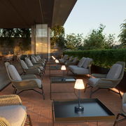 Moderne Tischleuchte Lola Slim 30 auf einem Terrassentisch, umgeben von gemütlichen Sitzgelegenheiten in einer stilvollen Außenumgebung, seitliche Perspektive.