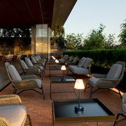 Moderne Tischleuchte Lola Slim 30 auf einem Terrassentisch, umgeben von gemütlichen Sitzgelegenheiten in einer stilvollen Außenumgebung, seitliche Perspektive.