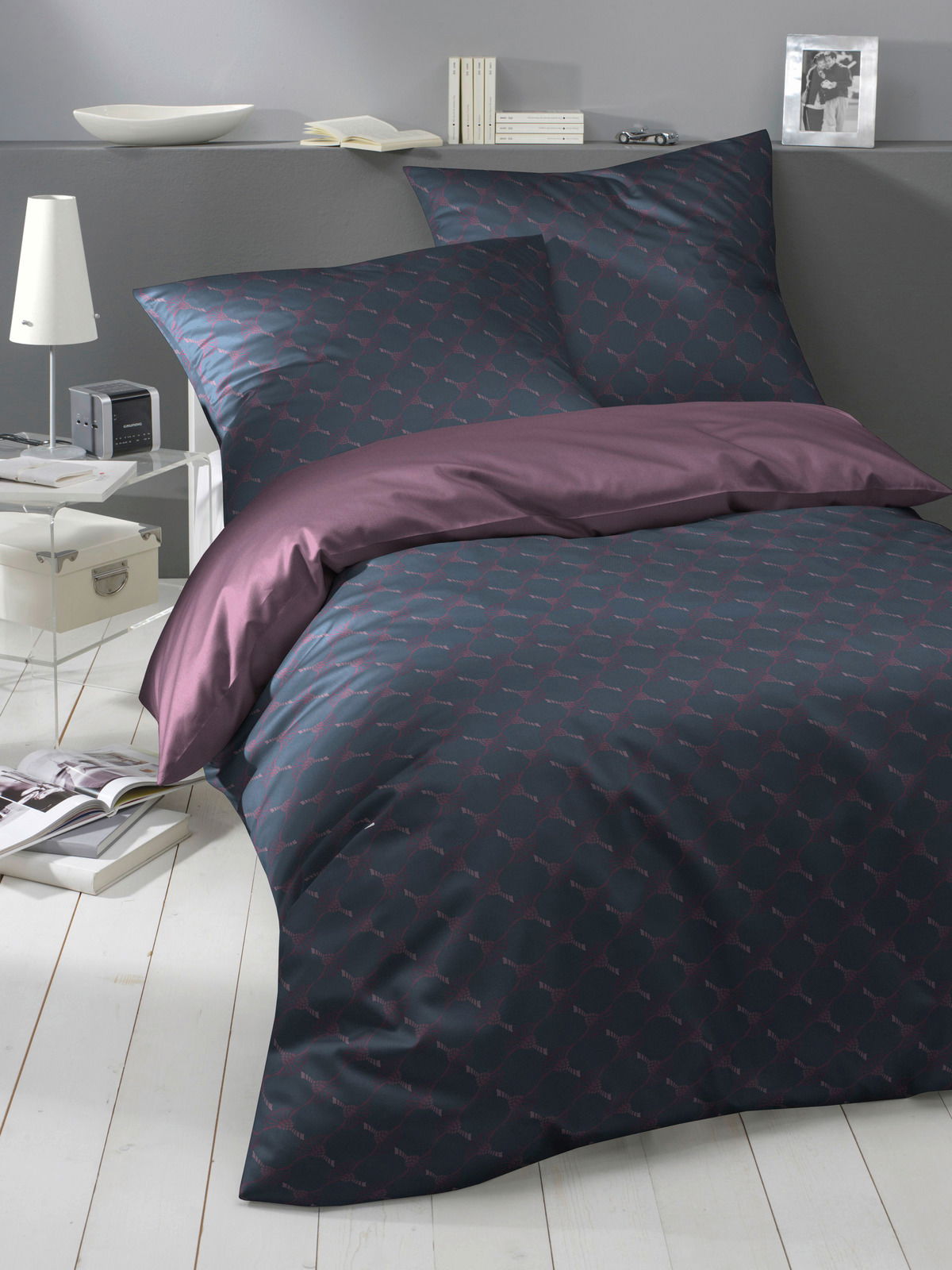Bettwäsche-Set in dunklem Design mit geometrischem Muster, bestehend aus Kissen- und Bettdeckenbezug, auf einem Bett in einem modern eingerichteten Raum, seitliche Perspektive