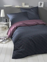 Bettwäsche-Set in dunklem Design mit geometrischem Muster, bestehend aus Kissen- und Bettdeckenbezug, auf einem Bett in einem modern eingerichteten Raum, seitliche Perspektive