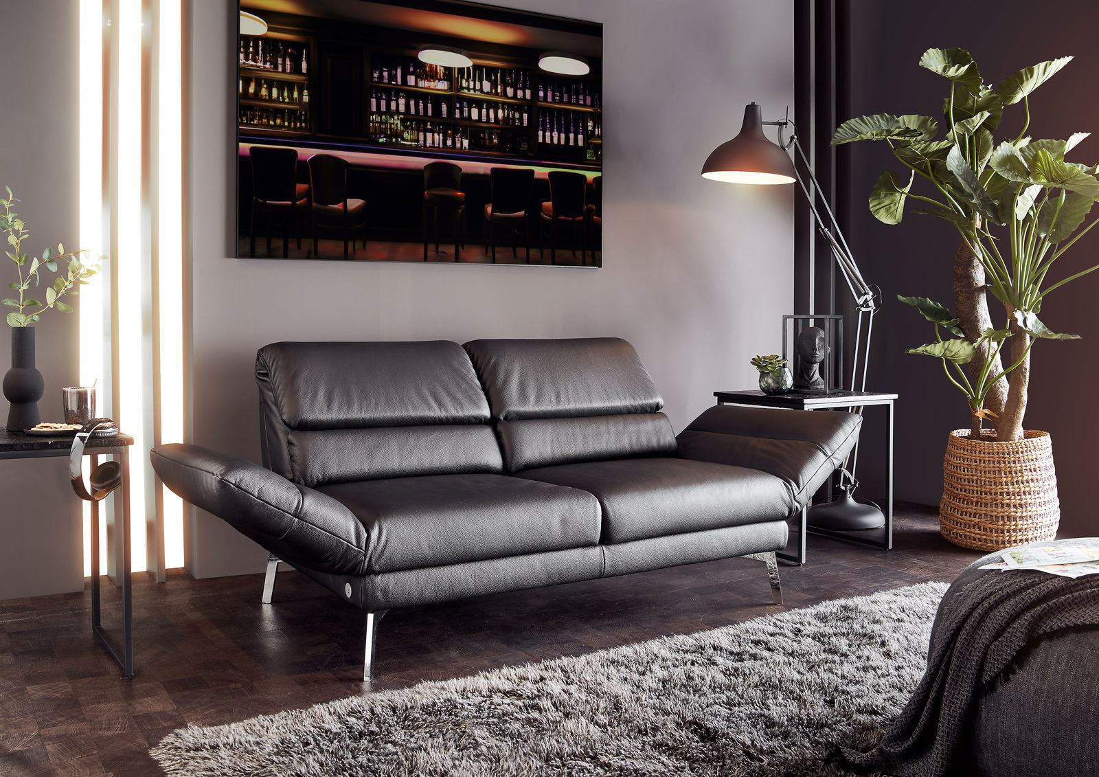 Modernes zweisitziges Sofa in schwarzem Leder, seitliche Perspektive, umgeben von stilvoller Dekoration und Pflanzen.