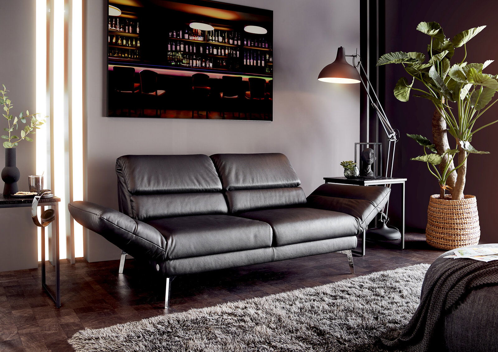 Dieter Knoll Sofa 2er COSIO Modernes zweisitziges Sofa in schwarzem Leder, seitliche Perspektive, umgeben von stilvoller Dekoration und Pflanzen.