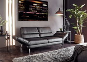 Modernes zweisitziges Sofa in schwarzem Leder, seitliche Perspektive, umgeben von stilvoller Dekoration und Pflanzen.