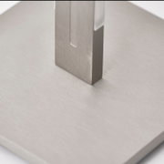 Detailansicht aus schräger Nahperspektive auf einen eckigen Metallfuß mit gebürsteter Oberfläche auf einer hellen Bodenplatte