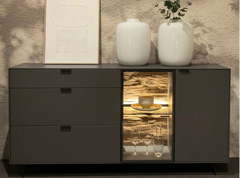 Dieter Knoll Sideboard RINA Modernes Sideboard mit drei Schubladen und einem beleuchteten Vitrinenfach, dekoriert mit zwei weißen Vasen und einem gerahmten Bild, frontal betrachtet.