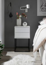 Moderne Nachtkommode mit geriffelter Oberfläche, dekoriert mit einer Vase und einer Uhr, aus frontaler Perspektive fotografiert.