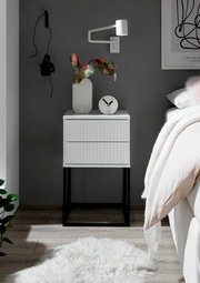 Moderne Nachtkommode mit geriffelter Oberfläche, dekoriert mit einer Vase und einer Uhr, aus frontaler Perspektive fotografiert.