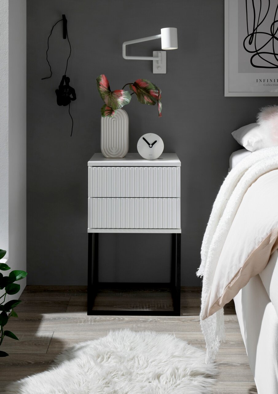 Moderne Nachtkommode mit geriffelter Oberfläche, dekoriert mit einer Vase und einer Uhr, aus frontaler Perspektive fotografiert.