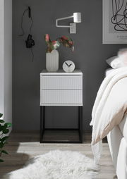 Moderne Nachtkommode mit geriffelter Oberfläche, dekoriert mit einer Vase und einer Uhr, aus frontaler Perspektive fotografiert.