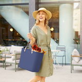 Frau in Sommerkleid und Hut trägt eine dunkelblaue Multibag Style 25l mit Blumen, seitliche Perspektive