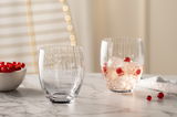 Zwei Trinkgläser POESIA 380ml auf einem Marmortisch, eines leer und eines mit Eiswürfeln und roten Beeren gefüllt, seitliche Perspektive.