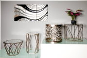 Modernes Wohn-Arrangement in Frontansicht: geometrische Metall- und Glas-Beistelltische/Podeste in Roségold-Optik auf Glasfläche, mit Pflanze und abstraktem Wandbild im Hintergrund