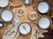 Rustikales Tisch-Arrangement aus der Vogelperspektive: mehrere weiß-blaue Keramikschalen mit goldfarbenem Besteck auf Holzbrettern, Leinentüchern und Holzoberfläche, ergänzt durch Teelichter und Untersetzer.