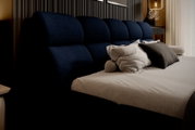 Seitliche Perspektive auf ein elegantes Polsterbett mit dunkelblauem Kopfteil und mehreren Kissen.