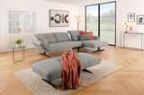 Großer grauer Hocker in einem modernen Wohnzimmer, mit einem roten Überwurf, auf einem Teppich vor einem Sofa. Perspektive von vorne.