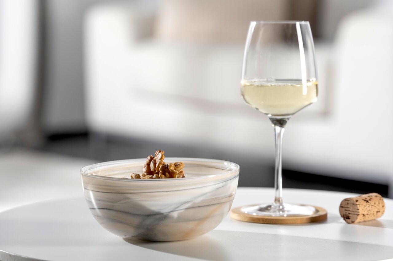 Beige-zwarte schaal ALABASTRO met walnoten, op een tafel naast een glas witte wijn en een kurk, zijaanzicht.
