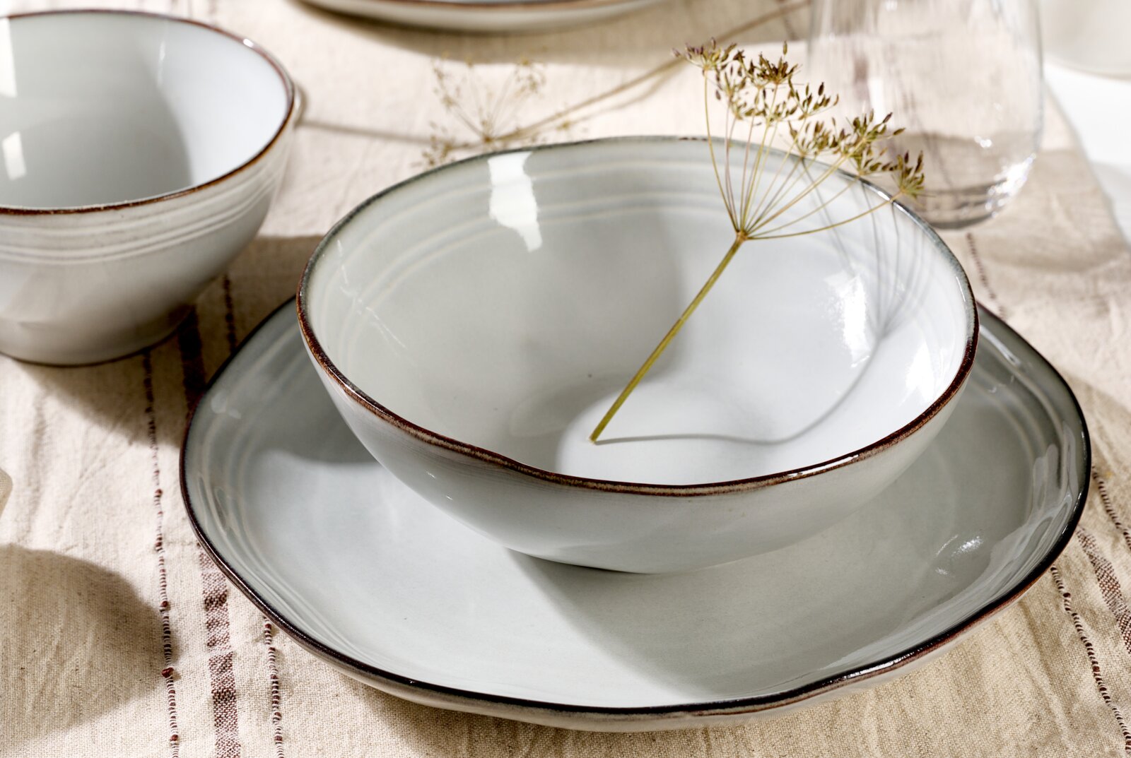 Nahaufnahme eines eleganten, 18-teiligen Tellersets mit schlichten, weißen Schalen und Tellern auf einem Tisch, dekoriert mit einem zarten Zweig.