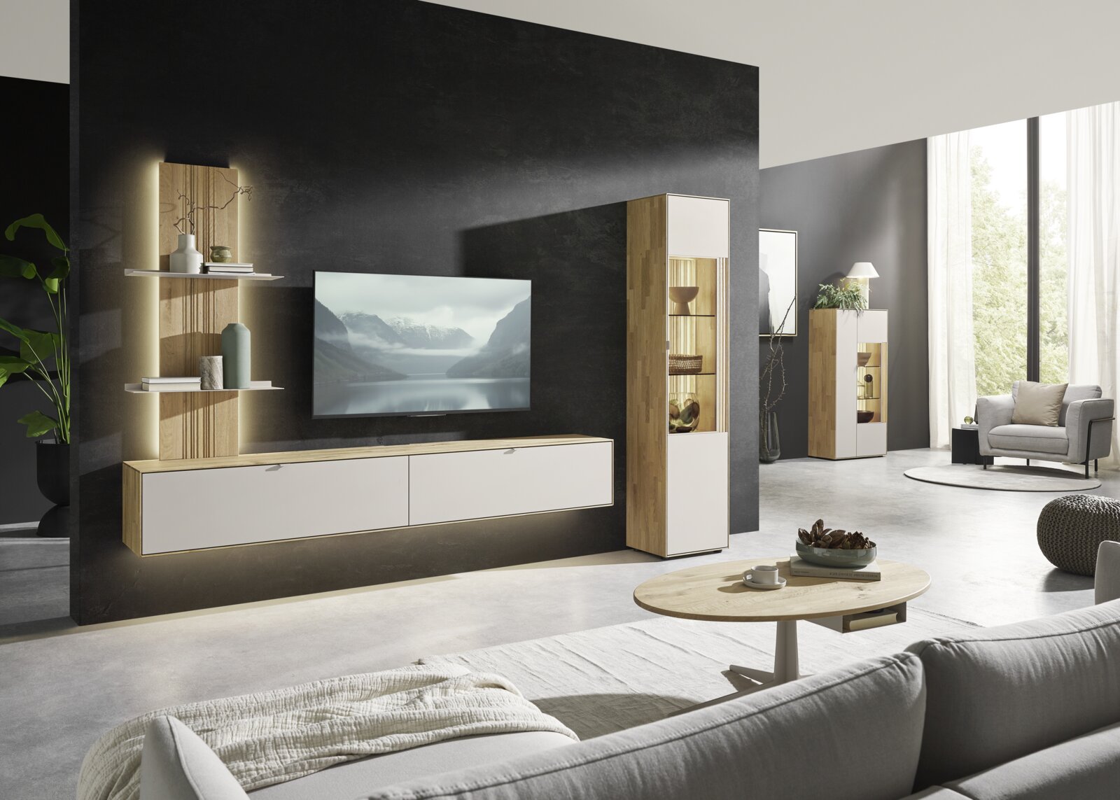 Dieter Knoll Highboard MALEA Modernes Wohnzimmer mit wandmontiertem TV-Lowboard in Holz-Optik und weißen Fronten, offenen Wandregalen und hoher Vitrine mit Glasfach und Beleuchtung; Ansicht aus leicht schräger Frontperspektive.