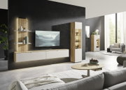 Modernes Wohnzimmer mit wandmontiertem TV-Lowboard in Holz-Optik und weißen Fronten, offenen Wandregalen und hoher Vitrine mit Glasfach und Beleuchtung; Ansicht aus leicht schräger Frontperspektive.