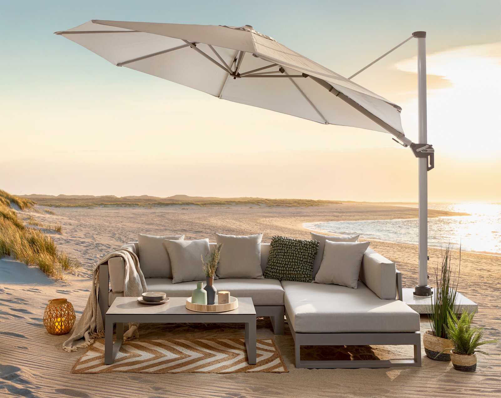 Een witte parasol met een zijdelingse paal boven een strandlounge bij zonsondergang, gefotografeerd vanuit een licht zijdelingse hoek van voren.