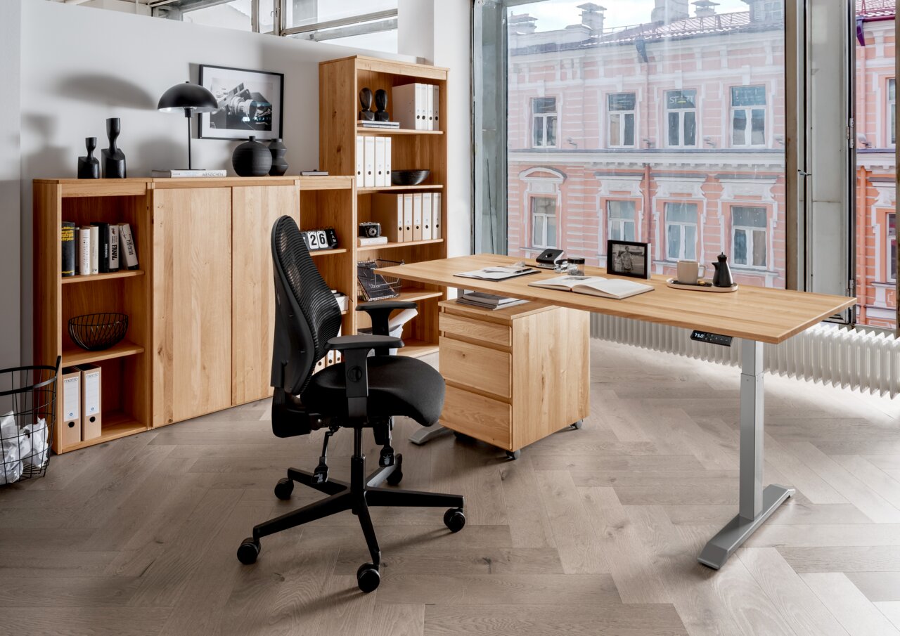 Moderne Büroumgebung mit einem höhenverstellbaren E-Schreibtisch aus Holz, einem schwarzen Bürostuhl und einem Aktenschrank, seitliche Perspektive.