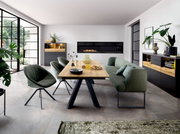 Moderne eetkamer met houten eettafel op zwart metalen onderstel, groene gestoffeerde stoelen en bank, en zwarte dressoirs met houtaccenten; perspectief: frontale, licht schuin van links genomen kameropname.