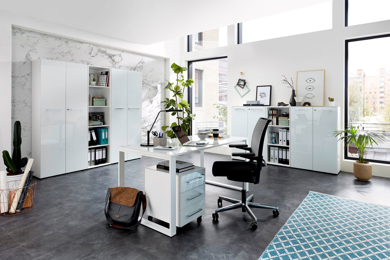 XORA Aktenschrank niedrig MATERNO Moderne Büroumgebung mit Schreibtisch, Rollcontainer und Aktenschränken in heller, minimalistischer Gestaltung. Perspektive: seitliche Ansicht des Schreibtischs mit Blick auf die Schränke im Hintergrund.