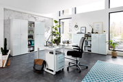 Moderne Büroumgebung mit Schreibtisch, Rollcontainer und Aktenschränken in heller, minimalistischer Gestaltung. Perspektive: seitliche Ansicht des Schreibtischs mit Blick auf die Schränke im Hintergrund.