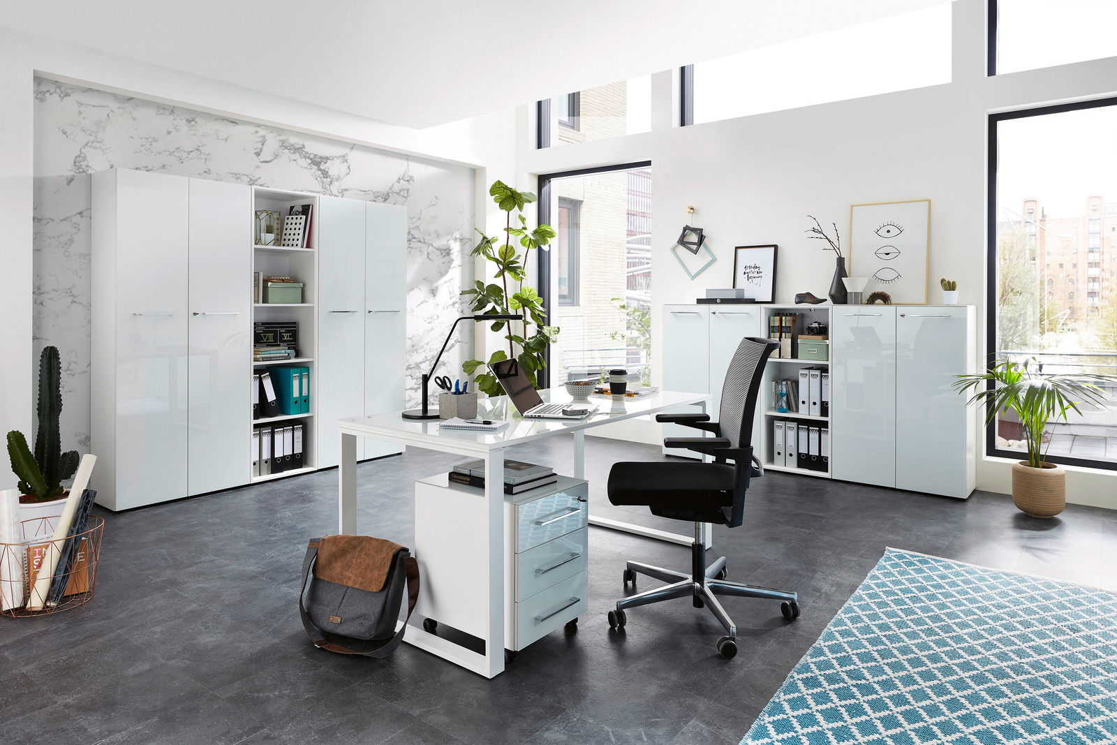 Moderne Büroumgebung mit Schreibtisch, Rollcontainer und Aktenschränken in heller, minimalistischer Gestaltung. Perspektive: seitliche Ansicht des Schreibtischs mit Blick auf die Schränke im Hintergrund.