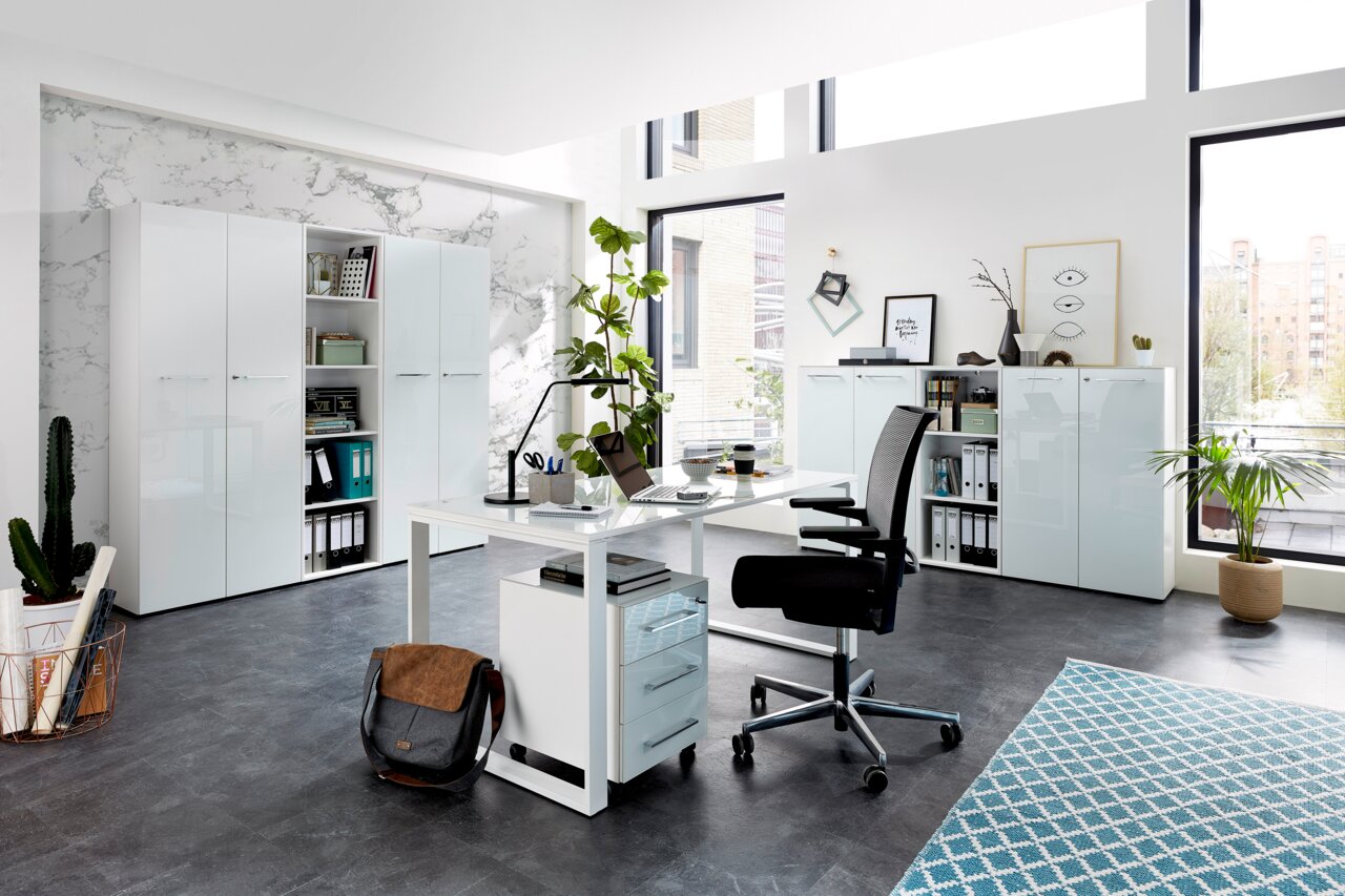 XORA Schreibtisch MATERNO Moderne Büroumgebung mit Schreibtisch, Rollcontainer und Aktenschränken in heller, minimalistischer Gestaltung. Perspektive: seitliche Ansicht des Schreibtischs mit Blick auf die Schränke im Hintergrund.