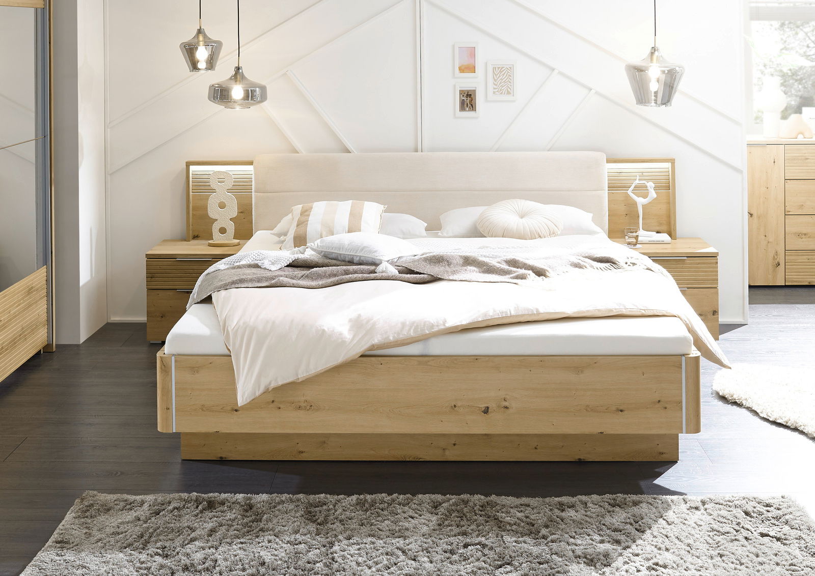 Frontale Ansicht einer modernen Bettanlage aus Holz mit hellem Kopfteil, flankiert von zwei Nachttischen und dekorativen Hängelampen.