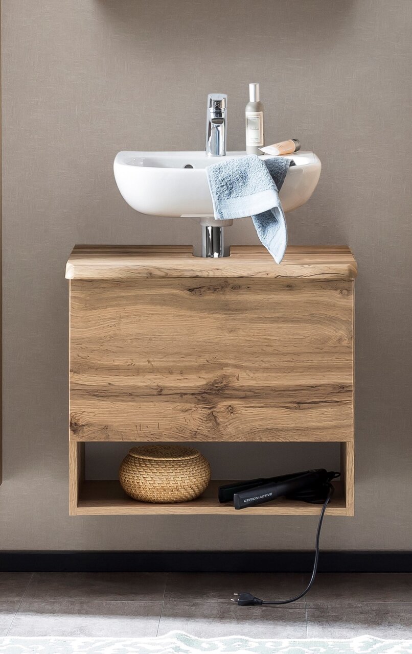 Waschbeckenunterschrank aus Holz mit integriertem Waschbecken, frontal fotografiert. Unter dem Schrank befindet sich ein offenes Fach mit einem Korb und einem Haarglätter.