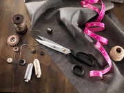 Schneiderschere 210 auf einem Tisch mit Nähzubehör, darunter Stoff, Maßband, Knöpfe und Garnrollen, aus der Vogelperspektive.