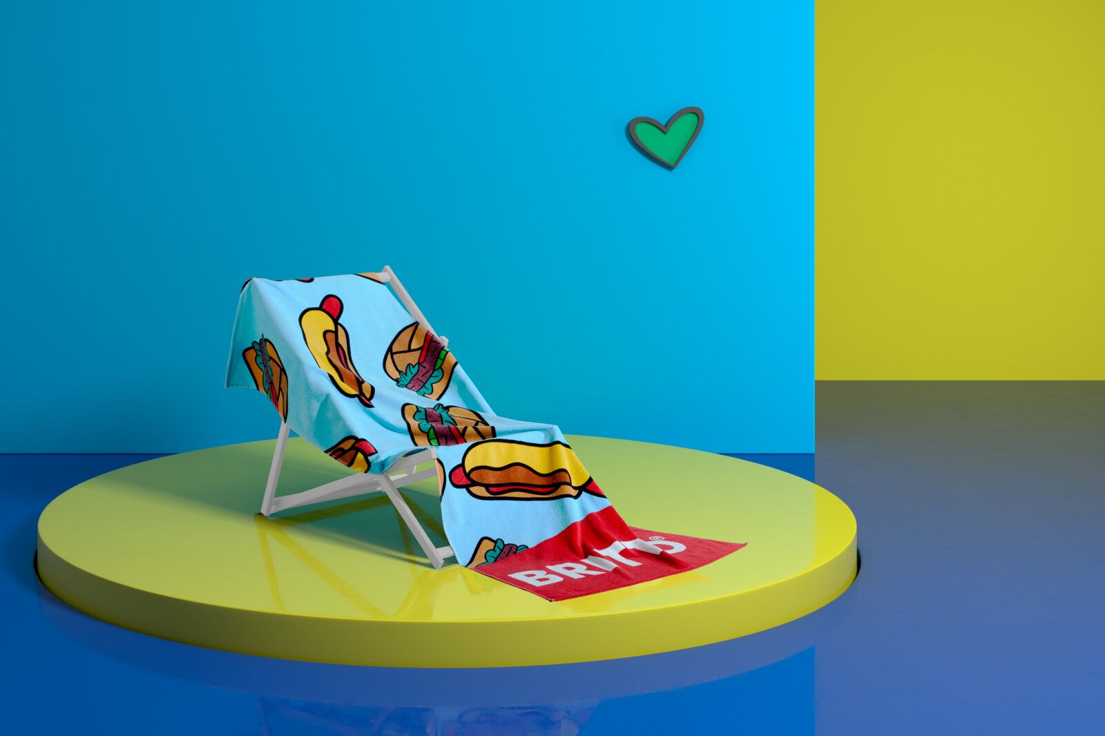 Ein buntes Velourstuch mit Hotdog- und Burger-Motiven liegt auf einem Liegestuhl, präsentiert auf einer runden Plattform vor einem zweifarbigen Hintergrund. Perspektive: seitlich.