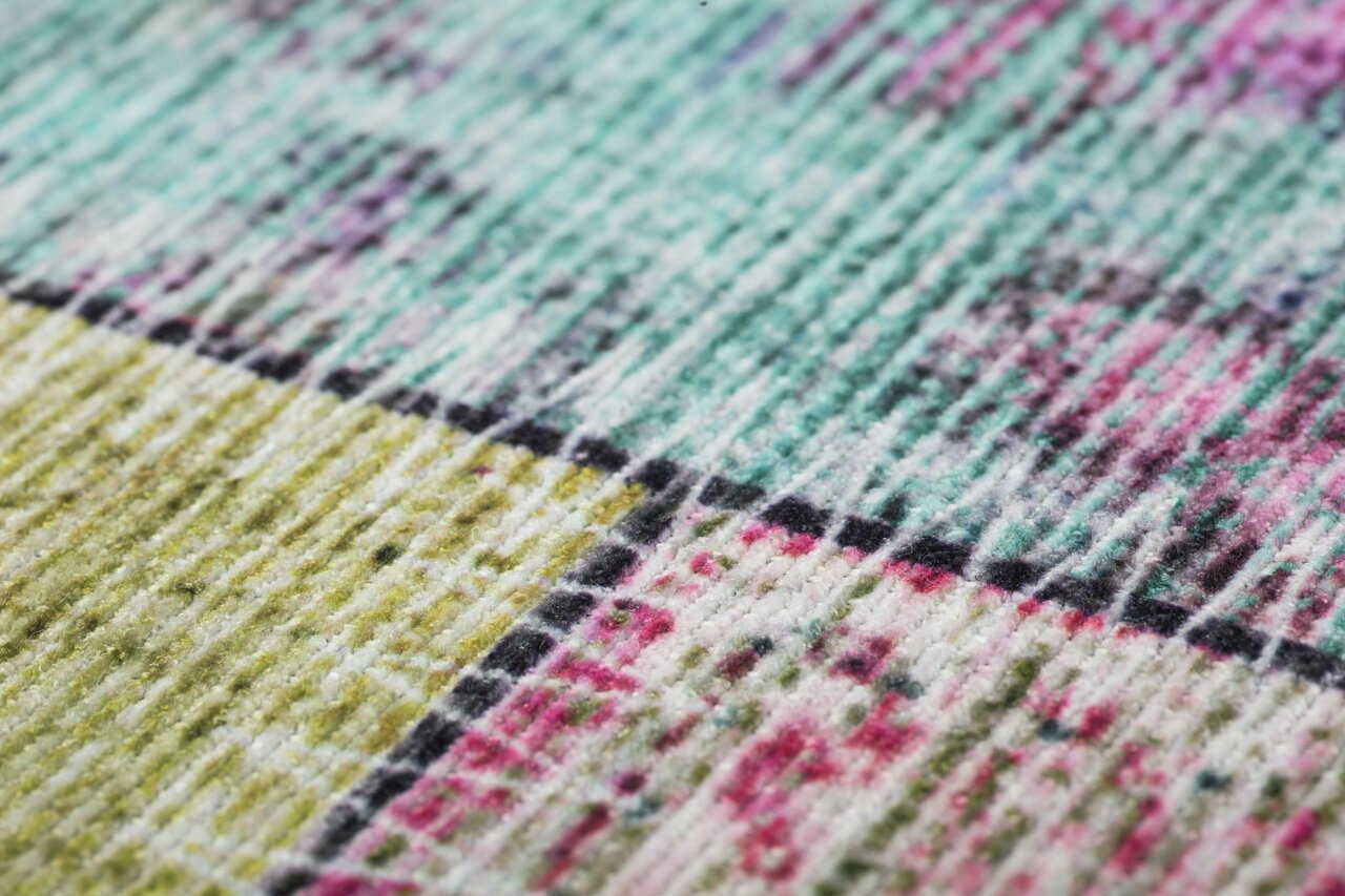 Nahaufnahme eines bunten Teppichs mit geometrischem Muster in Grün-, Blau- und Rosatönen, aus seitlicher Perspektive aufgenommen.