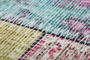 Nahaufnahme eines bunten Teppichs mit geometrischem Muster in Grün-, Blau- und Rosatönen, aus seitlicher Perspektive aufgenommen.