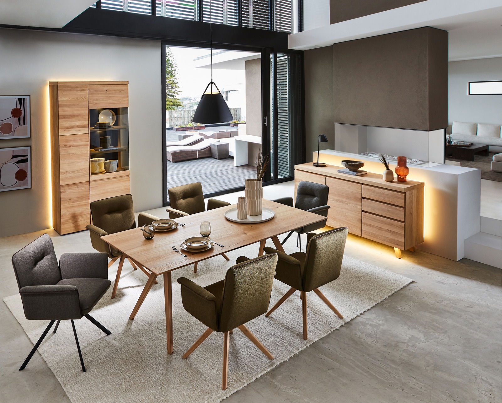 Moderne Esszimmermöbel mit Vitrine und Sideboard aus Holz, LED-Beleuchtung, Esstisch und gepolsterten Stühlen, seitliche Perspektive.