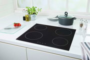 Moderne schwarze Glaskeramik-Kochplatte mit vier Kochzonen, umgeben von einer stilvollen weißen Küchenzeile. Perspektive von oben.