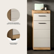 Schmaler Bad-Hochschrank/Unterschrank in Holzoptik mit vier weißen MDF-Schubladen (Rillenfräsung) und schwarzen Griffen, auf wasserresistenten Kunststofffüßen, frontal aus leicht seitlicher Perspektive fotografiert.