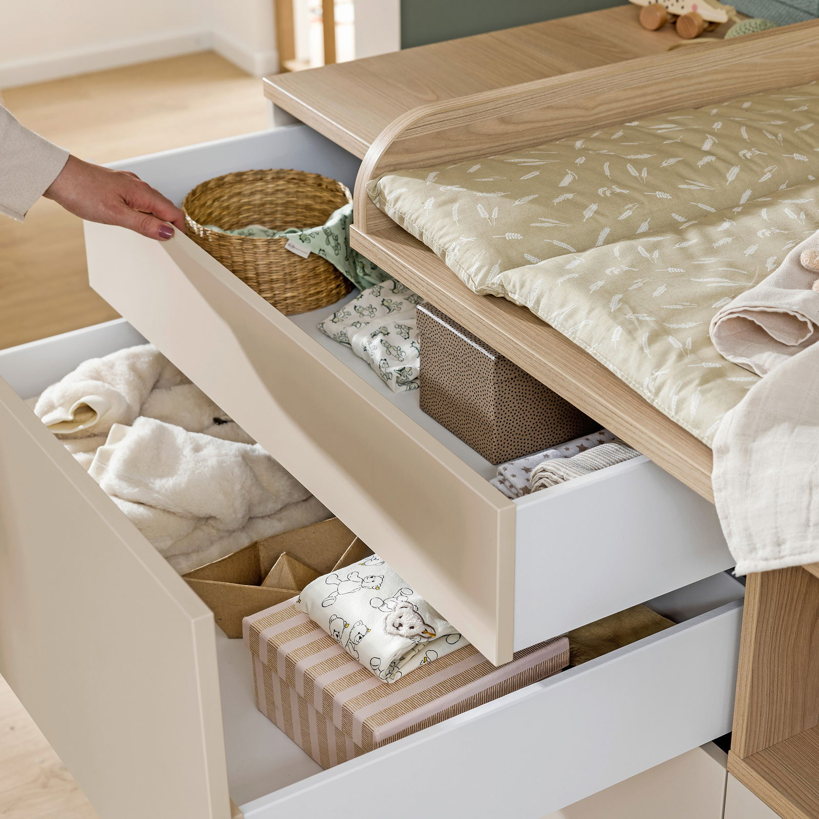 Kommode mit geöffneten Schubladen, gefüllt mit Babyartikeln, aus der Perspektive von oben betrachtet.