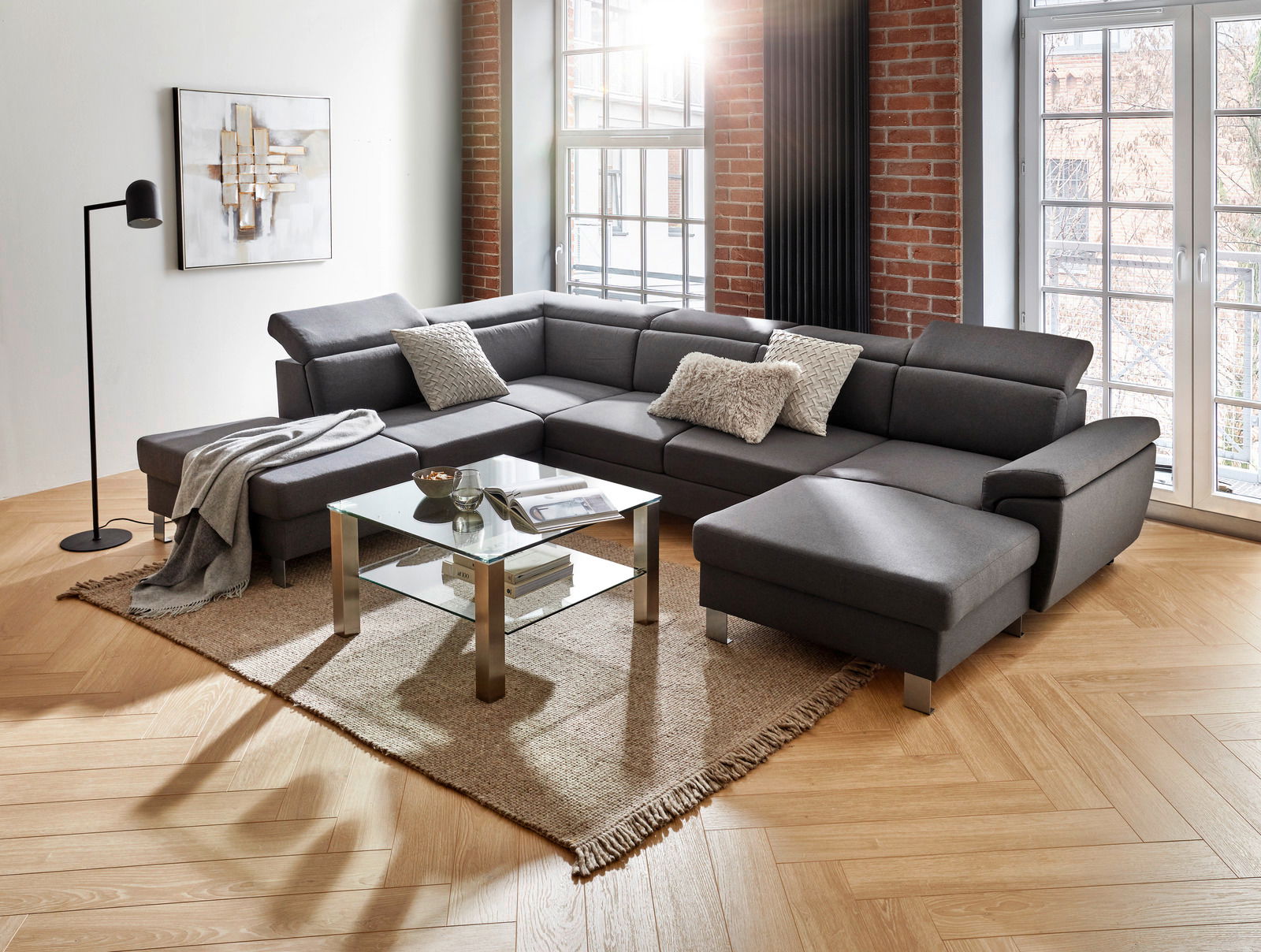 Moderne graue Rundecke in einem stilvollen Wohnzimmer mit großen Fenstern, Holzboden und Ziegelwand, aus der Perspektive von vorne links.