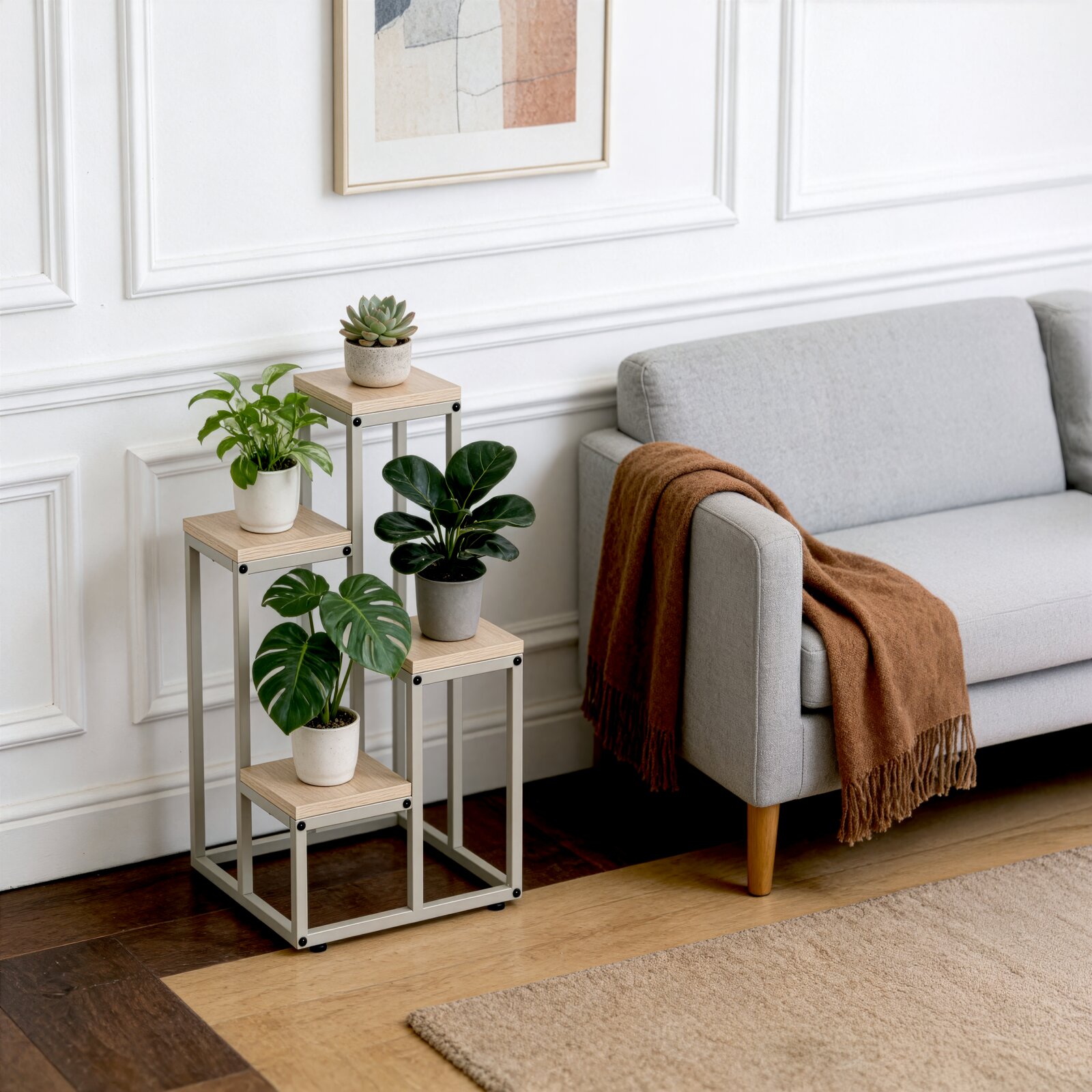 Modernes Pflanzenständer-Set mit drei unterschiedlich hohen Beistelltischen aus hellem Holz und grauem Metallgestell, dekoriert mit Topfpflanzen neben einem grauen Sofa perspektivisch in leicht schräger Frontansicht auf Augenhöhe aufgenommen.