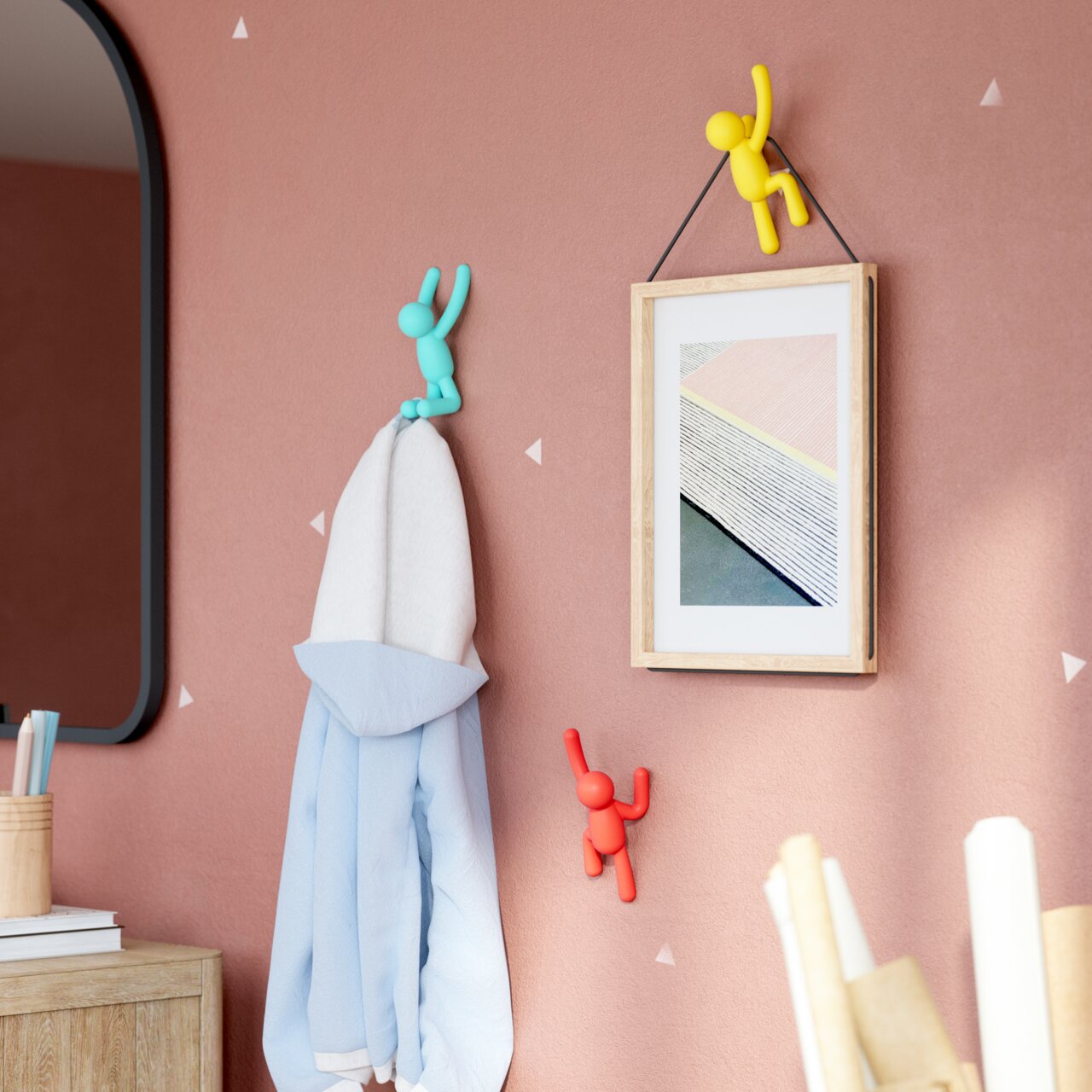 Wandhaken-Set BUDDY von Umbra in verschiedenen Farben, an einer Wand montiert, mit einem Handtuch und einem Bild, aus seitlicher Perspektive.