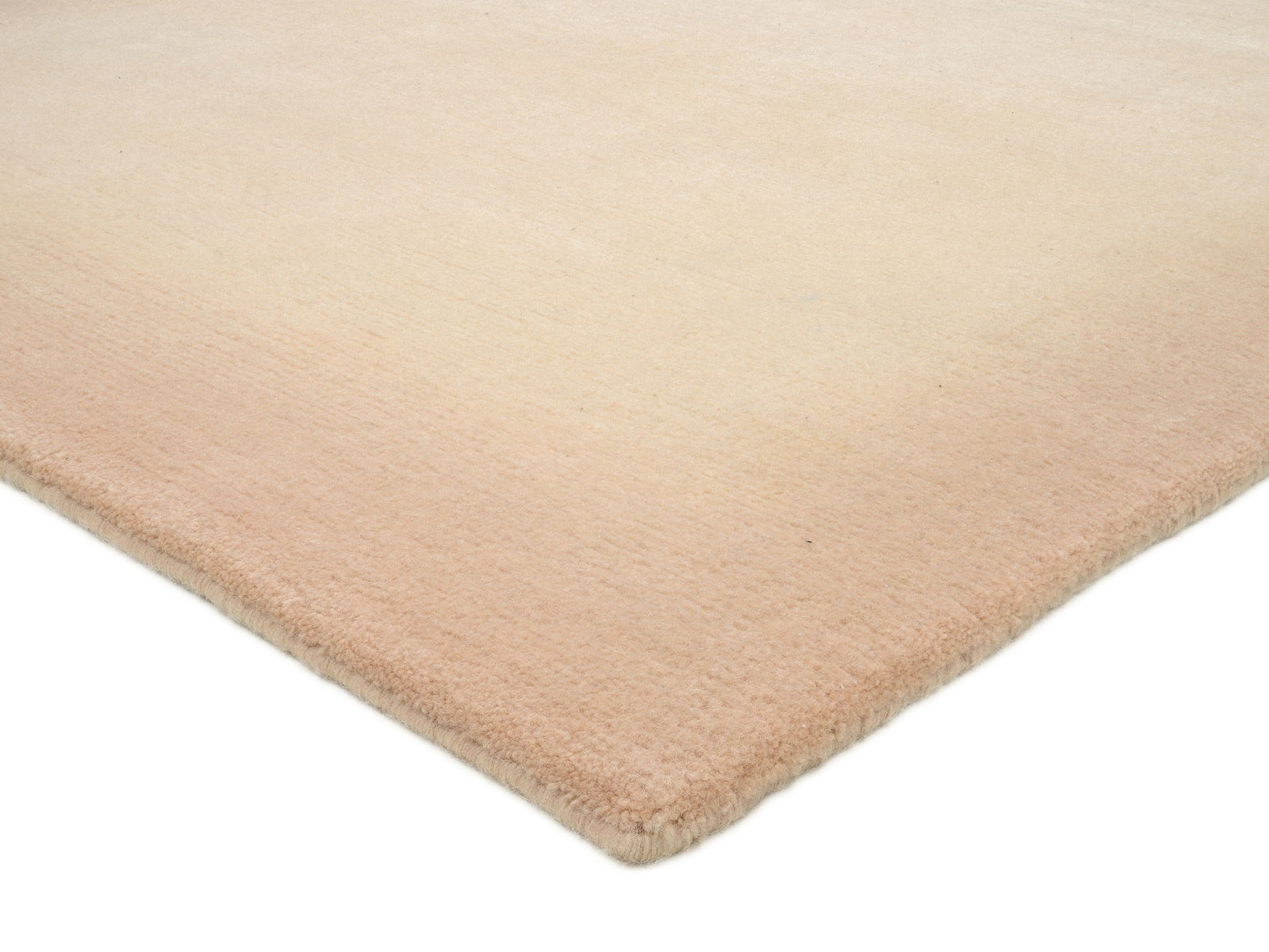 Ecke eines Wollteppichs in sanften Beige- und Rosatönen, aus der Perspektive von schräg oben fotografiert.