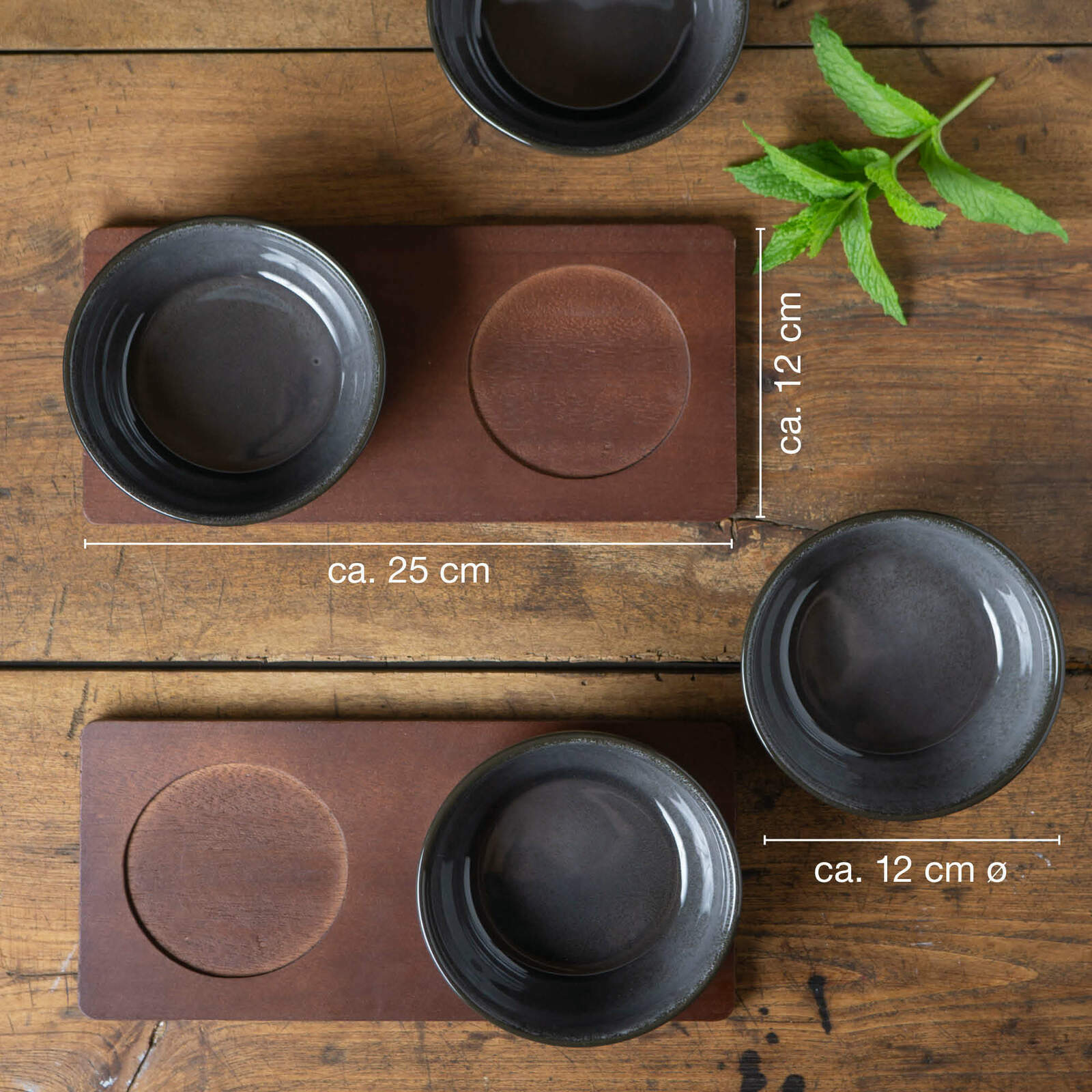 Vier anthrazitfarbene Miso-Schalen auf einem Holztisch, von oben betrachtet, mit zwei rechteckigen Untersetzern und einem Minzzweig.